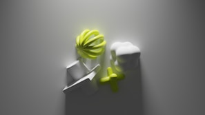 A minimalist composition featuring abstract shapes on a smooth surface. The central elements include a bright lime green spiral form, adjacent to a cloud-like white shape, and a cross-shaped object in green. The lighting creates soft shadows, enhancing the contrast and providing a sense of depth.