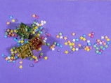 Multiple small, colorful star-shaped confetti pieces are scattered across a purple background. Three small gift boxes, decorated with green, red, and gold reflective surfaces and tied with gold string, are placed among the stars.