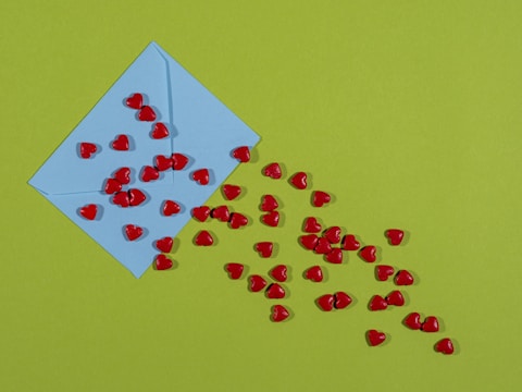 A blue envelope is positioned on a green surface with several small red heart-shaped objects scattered across and emerging from it.