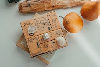 A collection of wooden stamps with intricate designs, including floral patterns and decorative symbols, is displayed on a light surface. The arrangement includes natural elements like seashells and a translucent rock. In the background, there are two brown pears and a piece of wood.