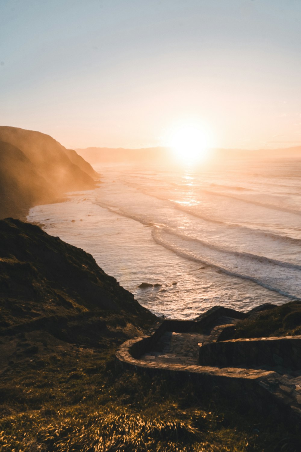 the sun is setting over the ocean with a path leading to the beach