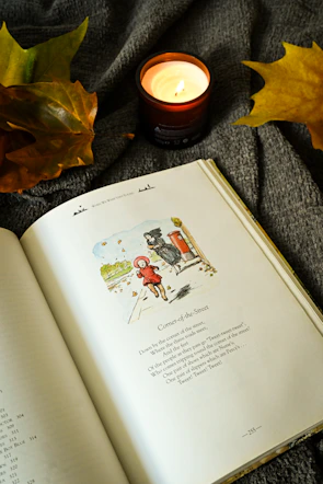 an open book sitting on top of a blanket next to a candle