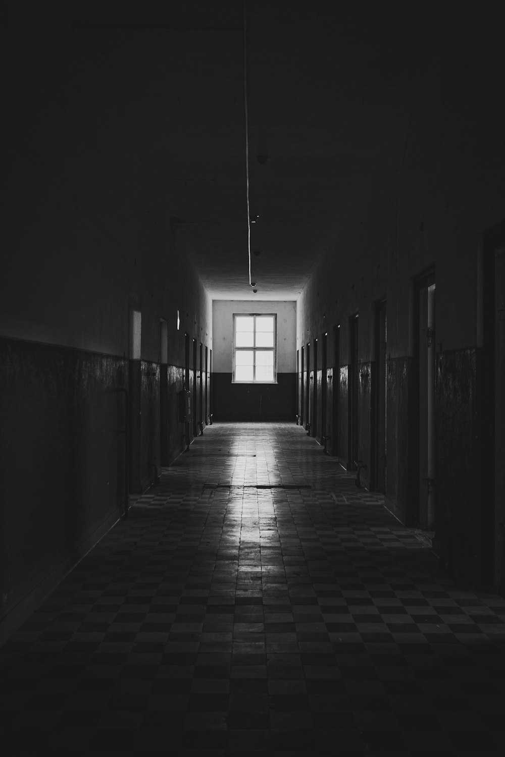 a dark hallway with a checkered floor and a window