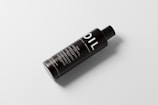 A sleek black bottle with the word 'OIL' prominently displayed in large white letters. The bottle has a simple, modern design with additional text details in smaller white font. It sits on a light, neutral background and casts a soft shadow, giving it a floating effect.