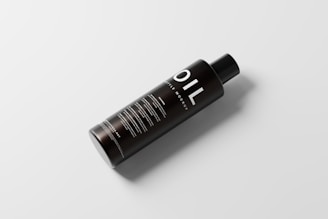 A sleek black bottle with the word 'OIL' prominently displayed in large white letters. The bottle has a simple, modern design with additional text details in smaller white font. It sits on a light, neutral background and casts a soft shadow, giving it a floating effect.