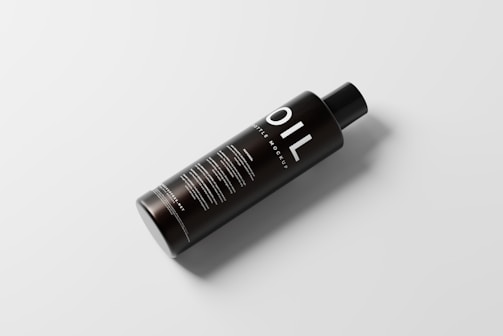 A sleek black bottle with the word 'OIL' prominently displayed in large white letters. The bottle has a simple, modern design with additional text details in smaller white font. It sits on a light, neutral background and casts a soft shadow, giving it a floating effect.