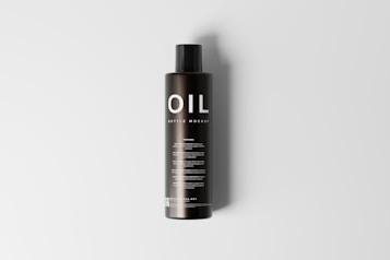 A tall, black cylindrical bottle with a sleek design is placed upright on a light gray background. The bottle features the word 'OIL' prominently displayed in large, white letters at the top, followed by the smaller text 'BOTTLE MOCKUP'. There are multiple lines of text below, which appear to provide additional details, likely about the product or its usage.