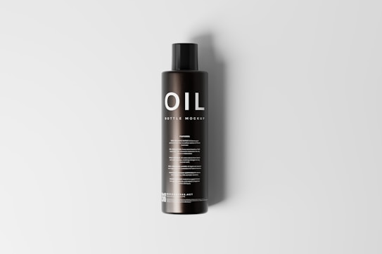 A tall, black cylindrical bottle with a sleek design is placed upright on a light gray background. The bottle features the word 'OIL' prominently displayed in large, white letters at the top, followed by the smaller text 'BOTTLE MOCKUP'. There are multiple lines of text below, which appear to provide additional details, likely about the product or its usage.
