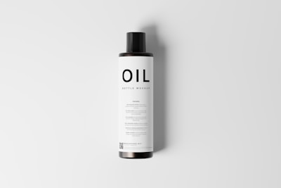 A cylindrical bottle mockup with a black cap and a minimalistic label displaying the word 'OIL' in bold letters. The label features additional text in smaller font, and a QR code is visible at the bottom. The bottle is presented against a plain, light gray background.