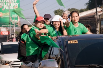 Happy children and parents waving beside a green and white mini bus in a neighborhood setting.