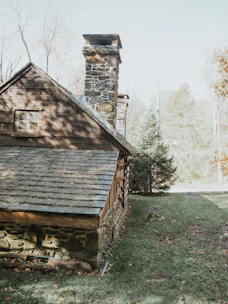 Charming rustic cabin nestled in the woods with a stone fireplace outside.