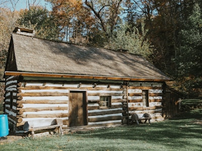a log cabin in the woods with a blue barrel next to it