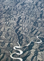 An aerial view of a rugged landscape with numerous ridges and valleys. A winding river snakes through the terrain, creating a stark contrast against the surrounding earth. The textures of the hills and the flowing river suggest a dramatic geological formation.