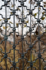a close up of a metal fence with a tree in the background