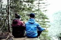 two people sitting on a rock in the woods