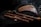 Several wooden wind instruments are arranged on a dark fabric background. The collection includes panpipes and various flutes with intricate designs. A subtle wisp of smoke adds to the atmosphere.