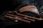Several wooden wind instruments are arranged on a dark fabric background. The collection includes panpipes and various flutes with intricate designs. A subtle wisp of smoke adds to the atmosphere.