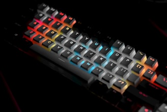 A mechanical keyboard with RGB backlighting, featuring keys in shades of red, blue, orange, and yellow, creating a vibrant, colorful effect against a dark background. Each key is individually lit, highlighting the letters and symbols prominently.