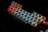 A mechanical keyboard with RGB backlighting, featuring keys in shades of red, blue, orange, and yellow, creating a vibrant, colorful effect against a dark background. Each key is individually lit, highlighting the letters and symbols prominently.