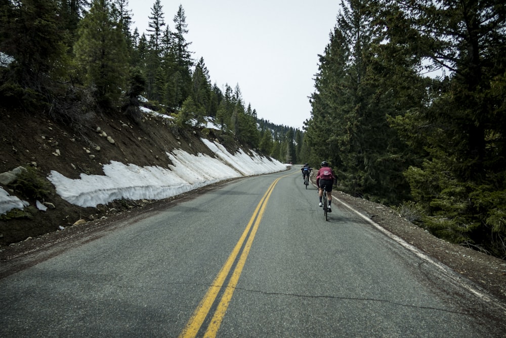 a couple of people riding bikes down a snow covered road