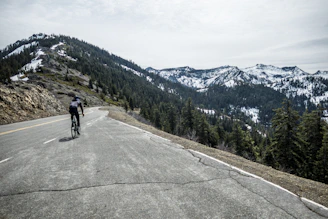 A cyclist navigating a scenic mountain road under a clear blue sky.