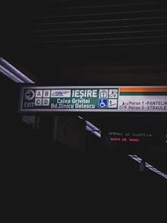 The image contains a directional sign in a transit area displaying various icons and text in Romanian indicating exits and platform numbers. The sign includes symbols for stairs, an elevator, and wheelchair accessibility, along with the names Calea Grivitei and Bd. Dinicu Golescu.
