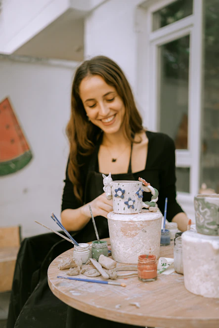 a woman sitting at a table painting a vase