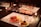 A table set with wine glasses and a variety of appetizers on white placemats. The appetizers include cured meats, cheese, and vegetables on plates. There are lit candles on the table and a bottle of wine in the center.