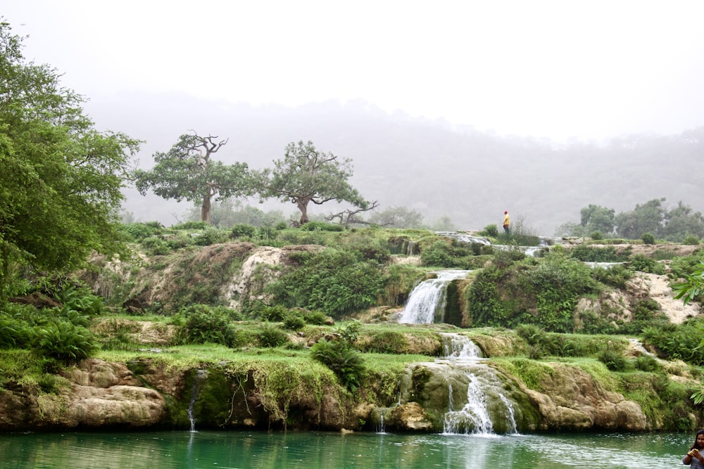 a man standing in the water next to a waterfall