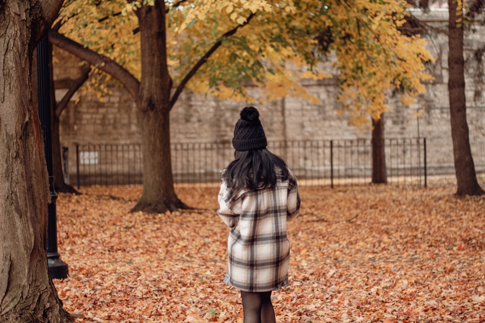a woman standing in a park with leaves on the ground