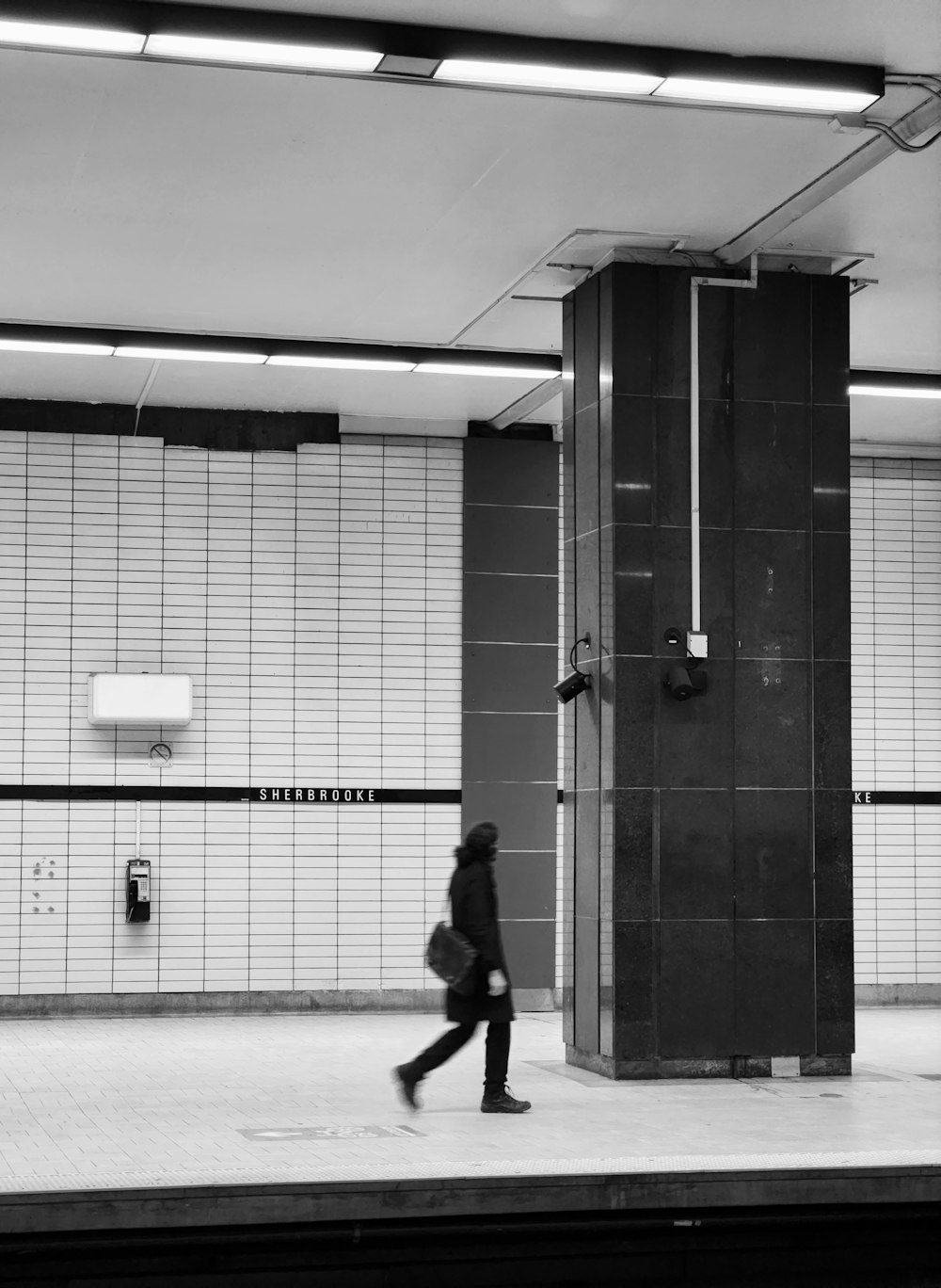 a black and white photo of a person walking on a subway platform