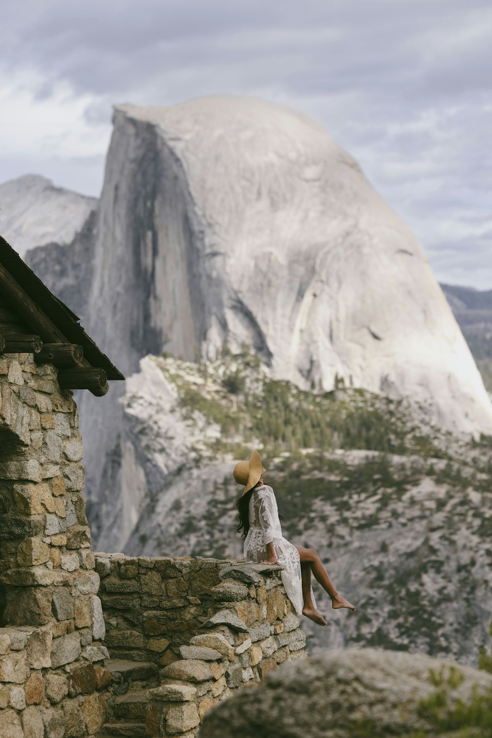a woman sitting on top of a stone wall next to a mountain