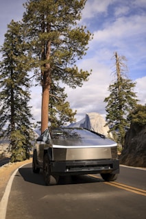 The Cybertruck carefully carrying a classic car on the deck trailer along a scenic highway.
