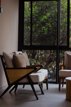 A cozy living room corner featuring a sleek wooden armchair with plush cushions bathed in warm natural light.