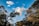 Trees with dense foliage are silhouetted against a bright blue sky with scattered fluffy clouds. A power line cuts diagonally through the scene, adding a contrast to the natural elements.