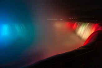 Nighttime view of Niagara Falls illuminated with colorful lights reflecting on the water.