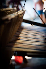Close-up of hands weaving silk threads on a traditional loom in warm natural light.