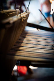 Close-up of hands weaving silk threads on a traditional loom in warm natural light.