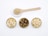 Three small round wooden bowls filled with various dried root slices are neatly arranged side by side. Above them, a wooden spoon rests on a ceramic dish, containing a small pile of beige powder. The items are placed on a clean white surface.