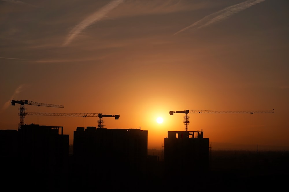 the sun is setting behind some construction cranes