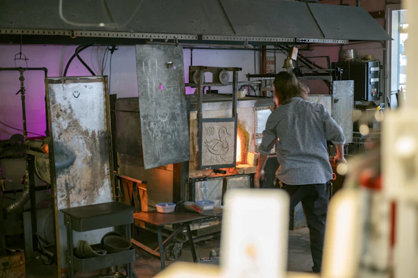 Artisan John Mailly carefully shaping a glass in his workshop filled with tools and raw materials