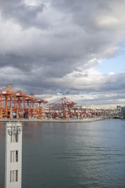 Drone flying over industrial port area at sunset with cranes and containers visible.