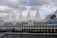 A large waterfront building with distinctive white sail-like structures on the roof, identified as Canada Place. The structure is adjacent to a body of water, with a cloudy sky in the background. The building's facade features glass windows and there is a mural visible on the side.