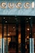 Glass storefront with sleek black doors, showcasing a luxurious and elegantly lit interior. The iconic brand name is prominently displayed above the entrance, set against a marble facade. Inside, there are upscale displays, plush furniture, and subtle lighting creating an opulent atmosphere.