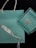 A Tiffany & Co. shopping bag and a matching box rest against a dark background. The box is open, revealing a silver necklace with a heart-shaped pendant. The iconic Tiffany blue color is prominent in both the bag and the box, complemented by white ribbon handles on the bag.