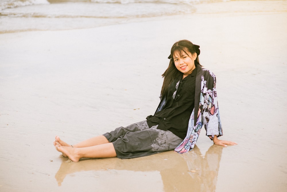 a woman sitting on the beach with her legs crossed