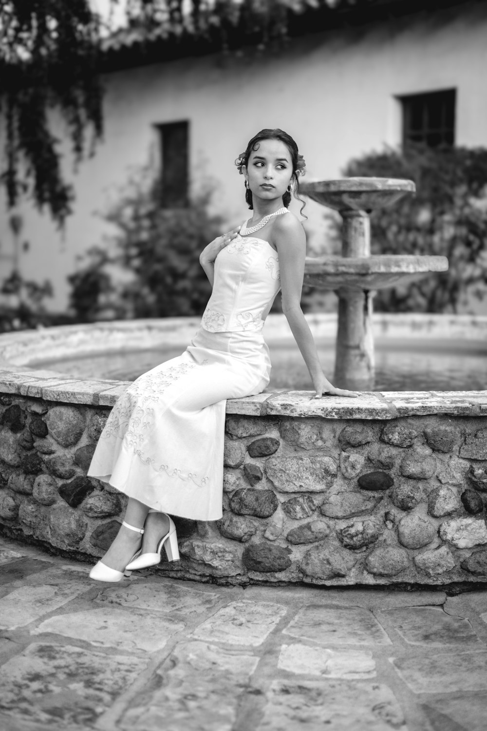 a woman in a white dress leaning on a fountain