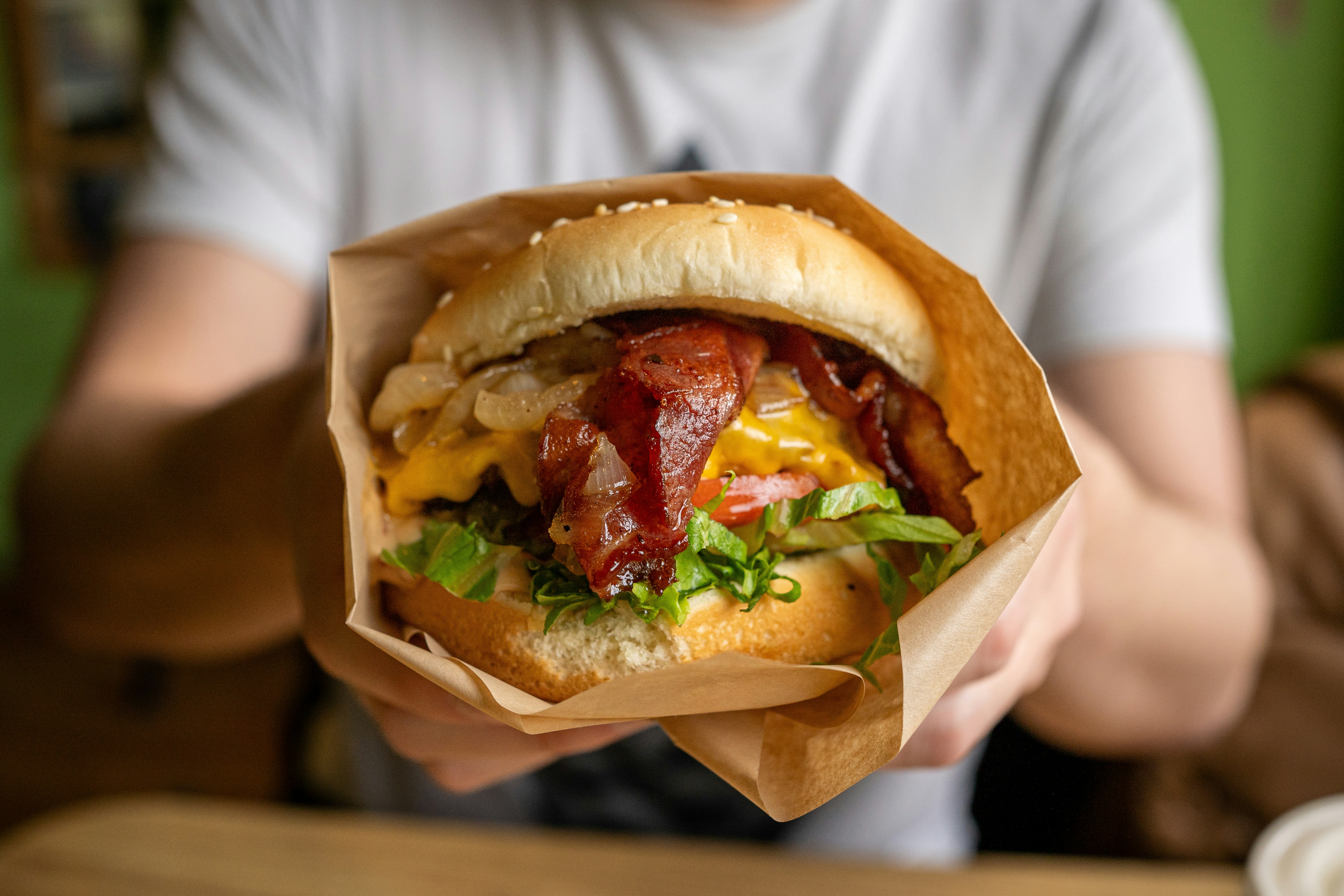 a person holding a sandwich with bacon and lettuce, The Roosevelt Burger from Rain City Burgers in Seattle