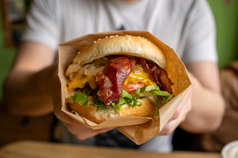 a person holding a sandwich with bacon and lettuce