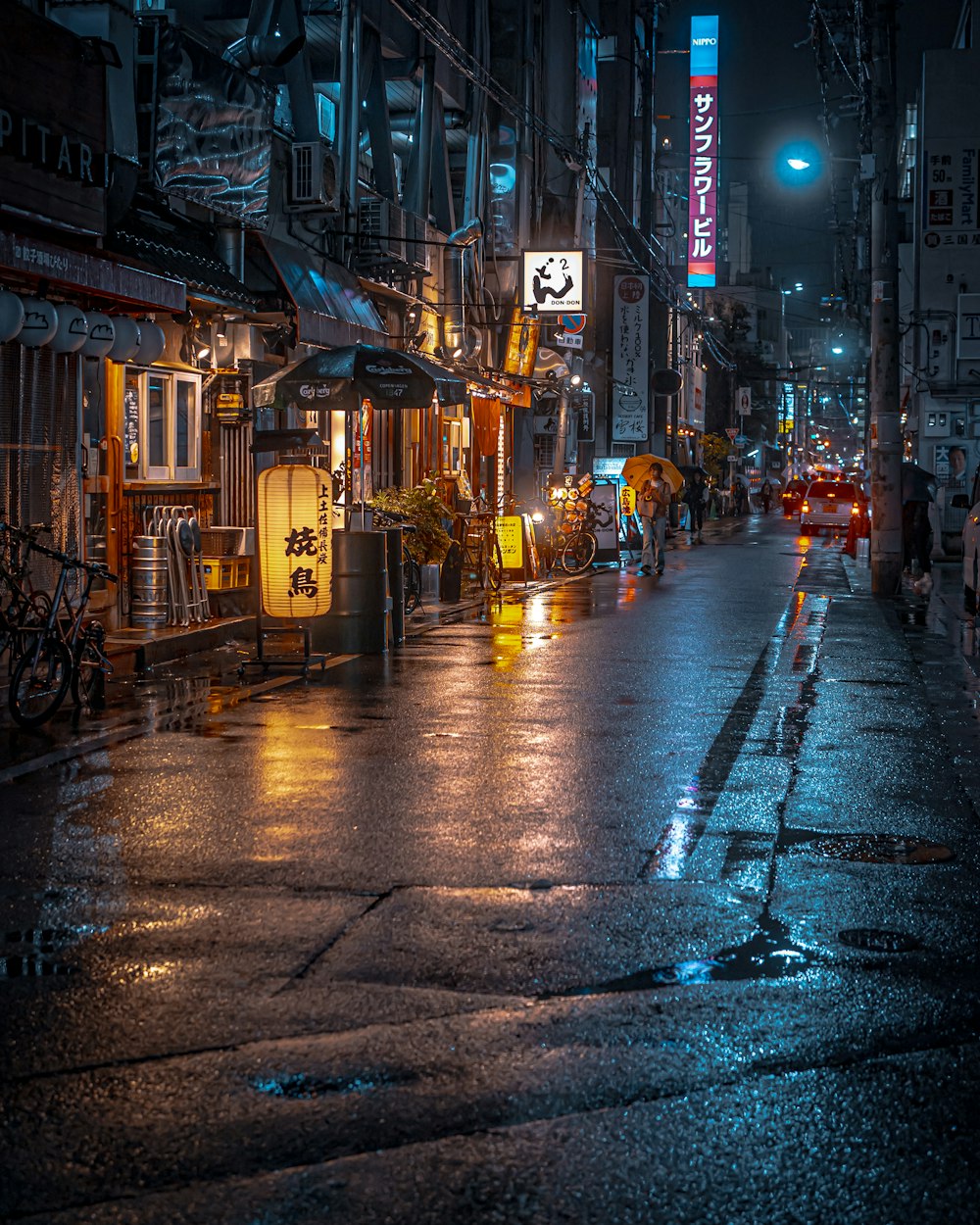 a wet city street at night with cars parked on the side of the road